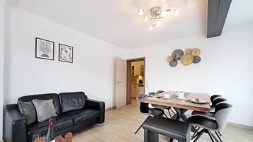 Ein modernes Wohnzimmer mit einem schwarzen Ledersofa, einem Esstisch mit Stühlen und einer Chandelier.