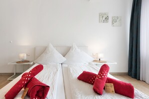 Quarto de hotel com duas camas, roupa de cama branca, toalhas vermelhas, abajures e uma obra de arte na parede.