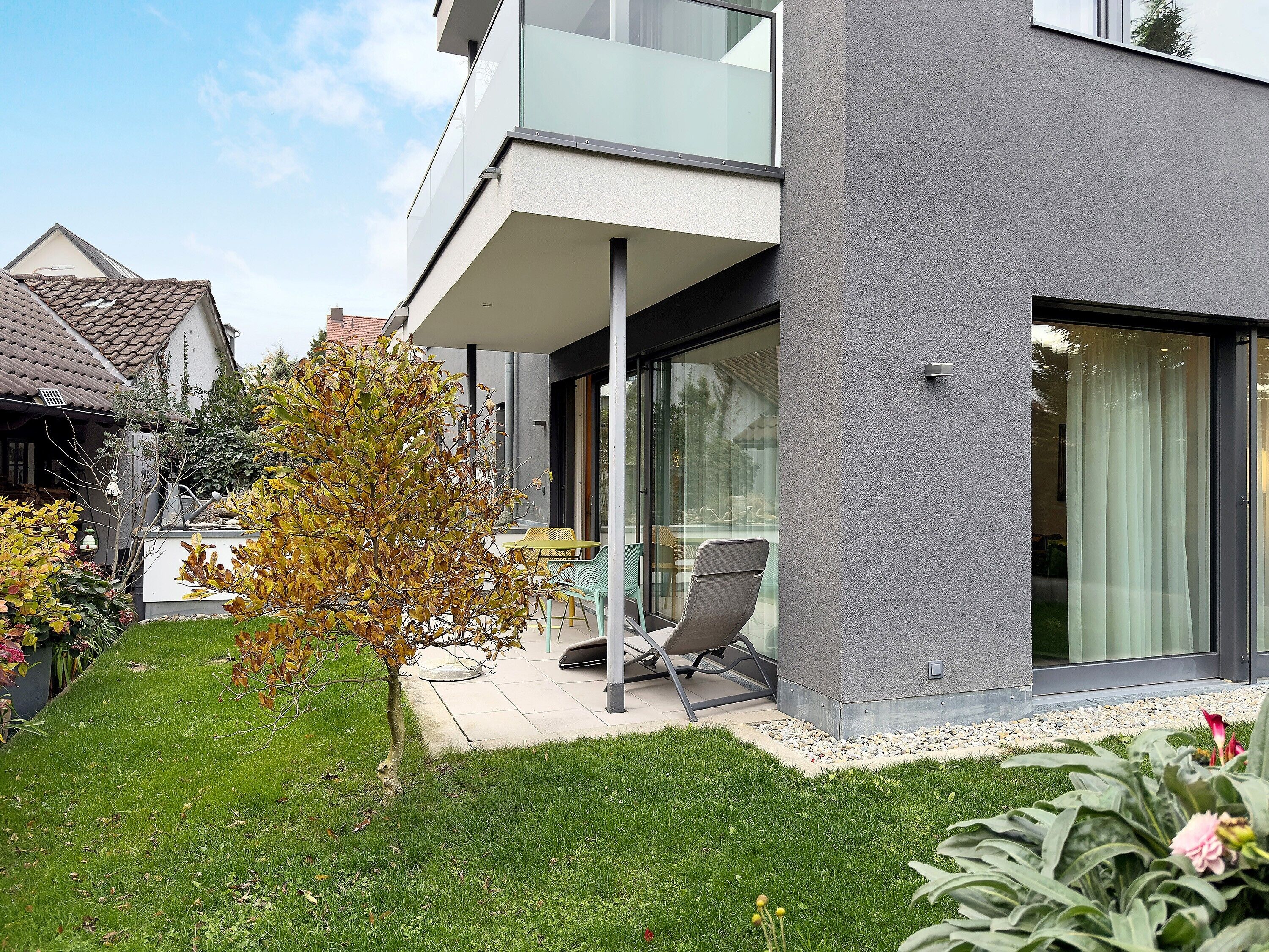 Ein modernes, zweistöckiges Haus mit Balkon, kleinem Garten und Terrassenbereich.