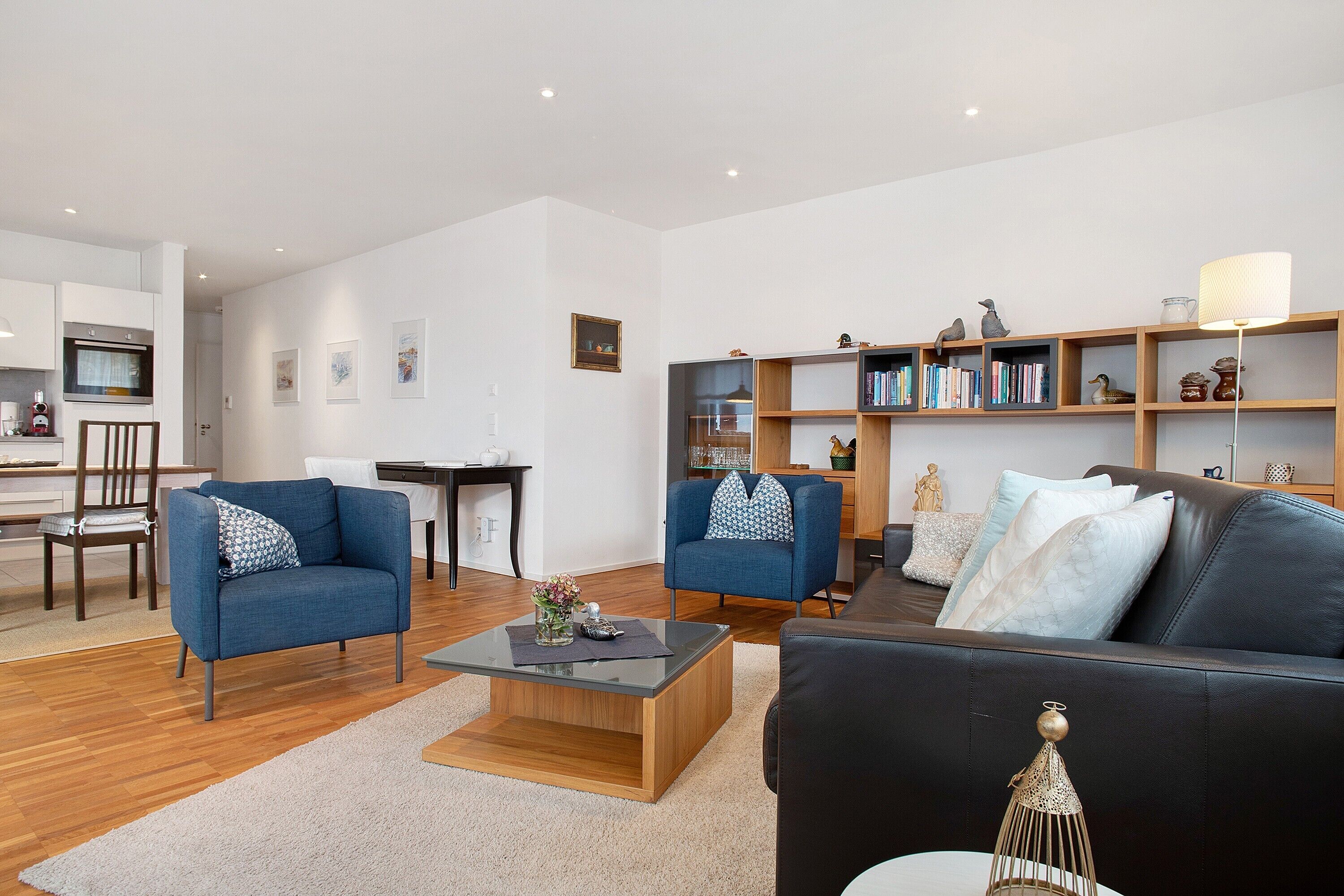 Ein modernes Wohnzimmer mit einer Couch, Sesseln, einem Couchtisch und einem Bücherregal.