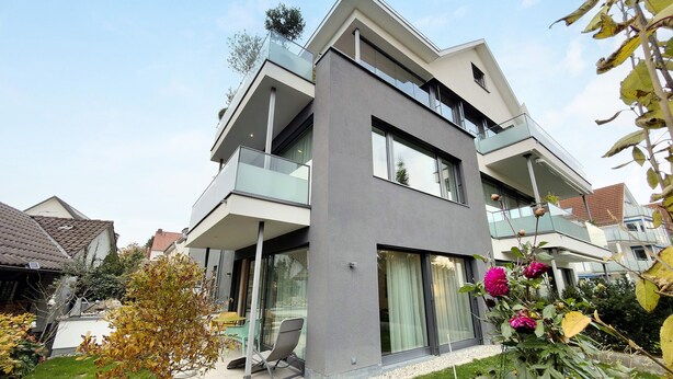 Een modern woongebouw met twee verdiepingen, een balkon, grote ramen en een verzorgde tuin.
