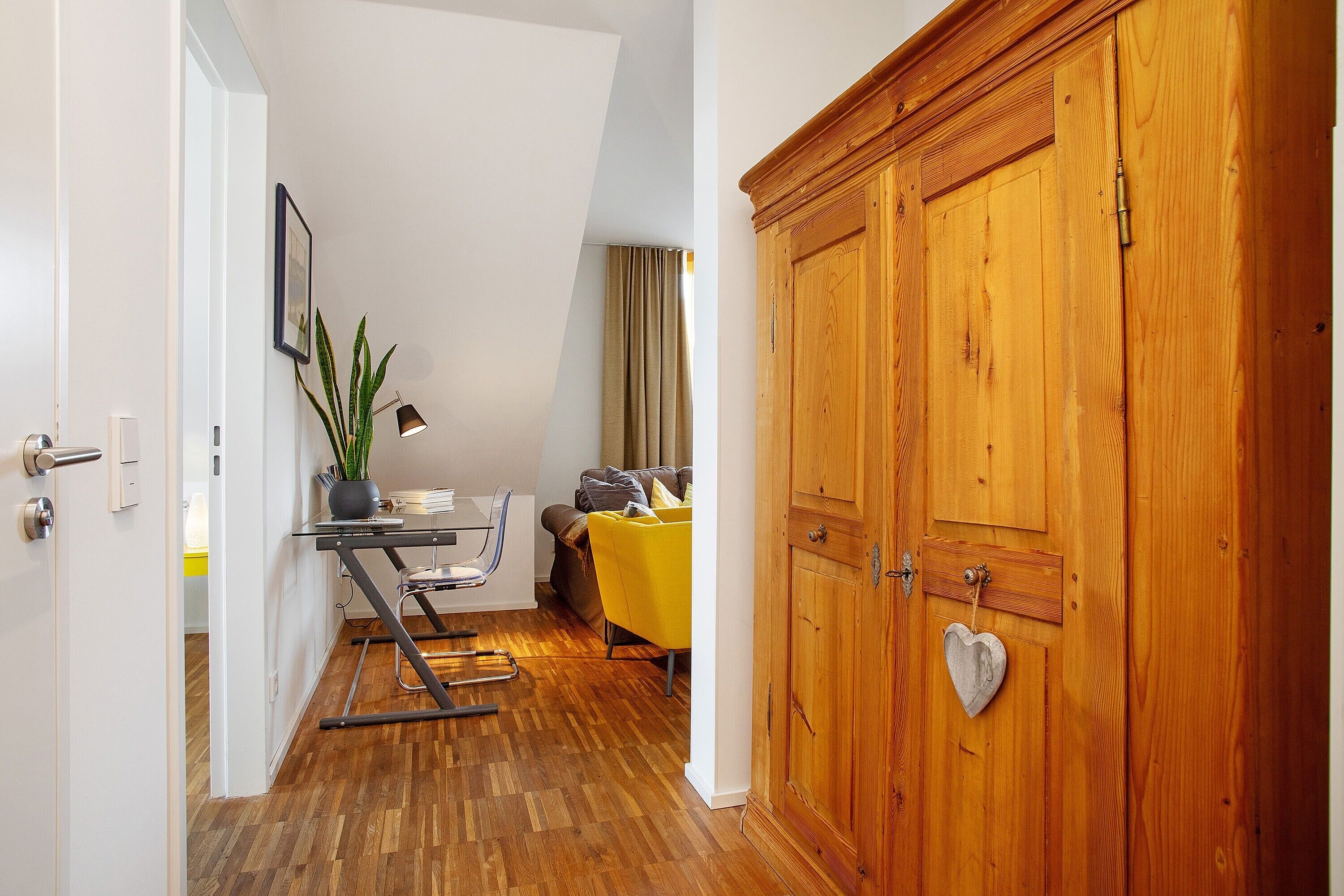 Ein Zimmer mit einem Holzschrank, einem Esstisch mit Stühlen, einer Couch und einer Zimmerpflanze.