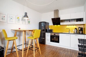 Une cuisine moderne équipée d’un réfrigérateur, d’un four et d’un four à micro-ondes. On y trouve une table à manger avec des chaises et un luminaire suspendu.