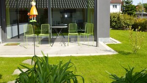 Een modern gebouw met een glazen deur, een terras met groene stoelen en een lamp.
