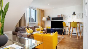 Een moderne woonkamer met een bank, gele stoelen, een glazen salontafel en een televisie.
