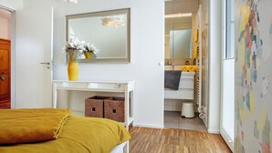 Een slaapkamer met een bed, nachtkastje, spiegel en een deur naar een badkamer.
