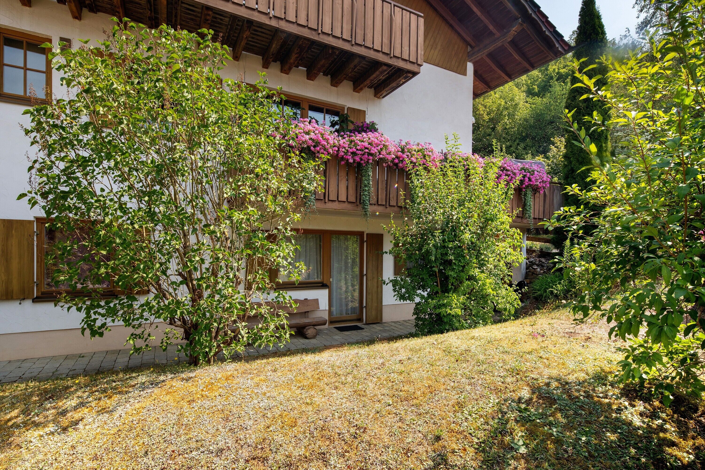 A two-story building with a wooden balcony, a bench, and a garden area with flowering plants.