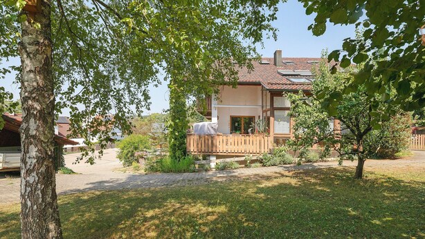 A house with a wooden deck, a covered outdoor seating area, and a garden with grass and trees.