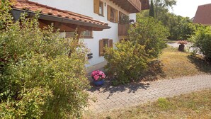 A traditional building with a tiled roof, wooden shutters, and a paved pathway leading to the entrance.
