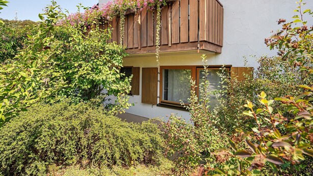 Ein zweistöckiges Gebäude mit einem Balkon, der mit blühenden Pflanzen bewachsen ist.