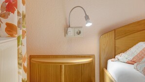 Ein Zimmer mit Nachttisch aus Holz, einer Wandleuchte und einem Bett mit weißem und orangefarbenem Kissen.