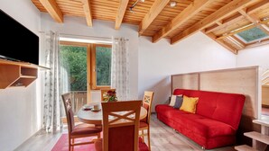 A room with a wooden ceiling, a red sofa, a dining table with chairs, and a TV mounted on the wall. - Apartment 'C' with Balcony and Wi-Fi (Lonsee)