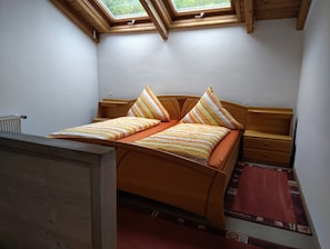 Een slaapkamer met een houten bed, dakraam, nachtkastje en een rood tapijt.