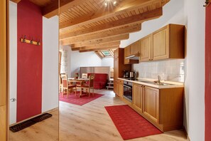 A modern kitchen with wooden cabinets, a red rug, and a dining area with a table and chairs.