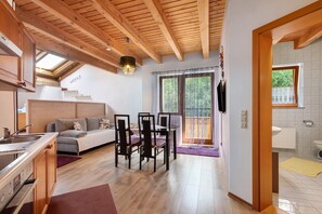A modern kitchen with wooden beams, a dining area with a sofa and chairs, and a large window with curtains.
