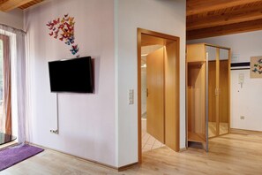 A hotel room with a flat-screen TV mounted on the wall, a wooden door, and a tiled floor.