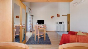 A cozy living room with a wooden ceiling, a dining area with a table and chairs, a television, and a small kitchenette with a microwave. - Apartment 'G' with Balcony and Wi-Fi (Lonsee)