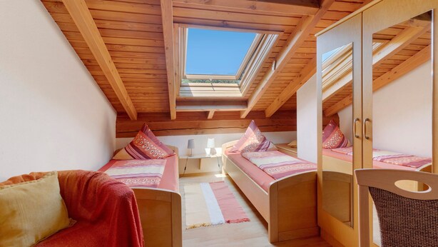 A compact room with a sloped ceiling, wooden beams, and a skylight. There are two beds with matching bedding and pillows. - Apartment 'G' with Balcony and Wi-Fi (Lonsee)