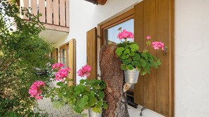 A building with wooden shutters, a tree trunk with hanging flower pots, and pink flowers. - Apartment 'G' with Balcony and Wi-Fi (Lonsee)