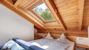 A bedroom with a sloped ceiling, a skylight, a bed with floral bedding, a blue sofa, and a bedside table. - Apartment 'H' with Balcony and Wi-Fi (Lonsee)