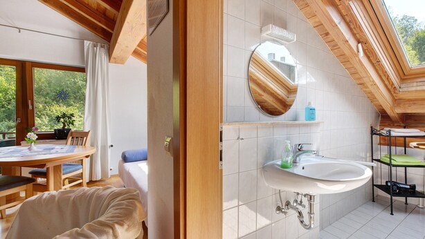 A room with a wooden ceiling, a round mirror, a white sink, and a dining area with a table and chairs. - Apartment 'H' with Balcony and Wi-Fi (Lonsee)