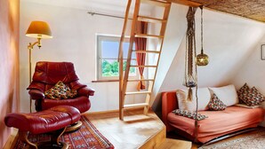 Una habitación con un sillón de cuero rojo, una escalera de madera, un sofá con cojines estampados, una lámpara colgante y una ventana con vistas.