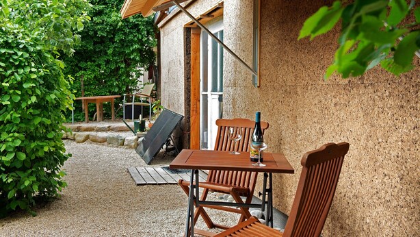 Un espacio de estar al aire libre con madera, una mesa, sillas, una botella de vino y una computadora portátil.