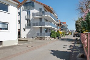 A multi-story residential building with balconies, a paved street, and a clear sky. - Apartment Type A with 28 sqm for 1-2 Persons (Immenstaad am Bodensee)