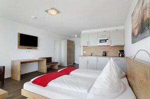 Una habitación de hotel moderna con cama, escritorio, televisión, kitchenette y un cuadro en la pared.