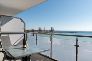Un balcon avec une table en verre, une bouteille de vin blanc et une vue dégagée sur la mer, avec une jetée en arrière-plan.