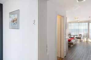 Una habitación de hotel moderna con cama, un pequeño rincón de descanso, una mesa de comedor y un amplio ventanal con cortinas.
