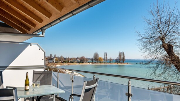 A balcony with a table and chairs, overlooking a body of water and a distant shoreline. - Apartment 'Typ A2' with Shared Terrace, Shared Garden and Wi-Fi (Immenstaad am Bodensee)