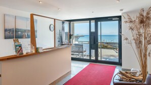A reception area with a red carpet, a wooden reception desk, a clock, and a view of the sea through a glass door. - Apartment 'Typ A2' with Shared Terrace, Shared Garden and Wi-Fi (Immenstaad am Bodensee)