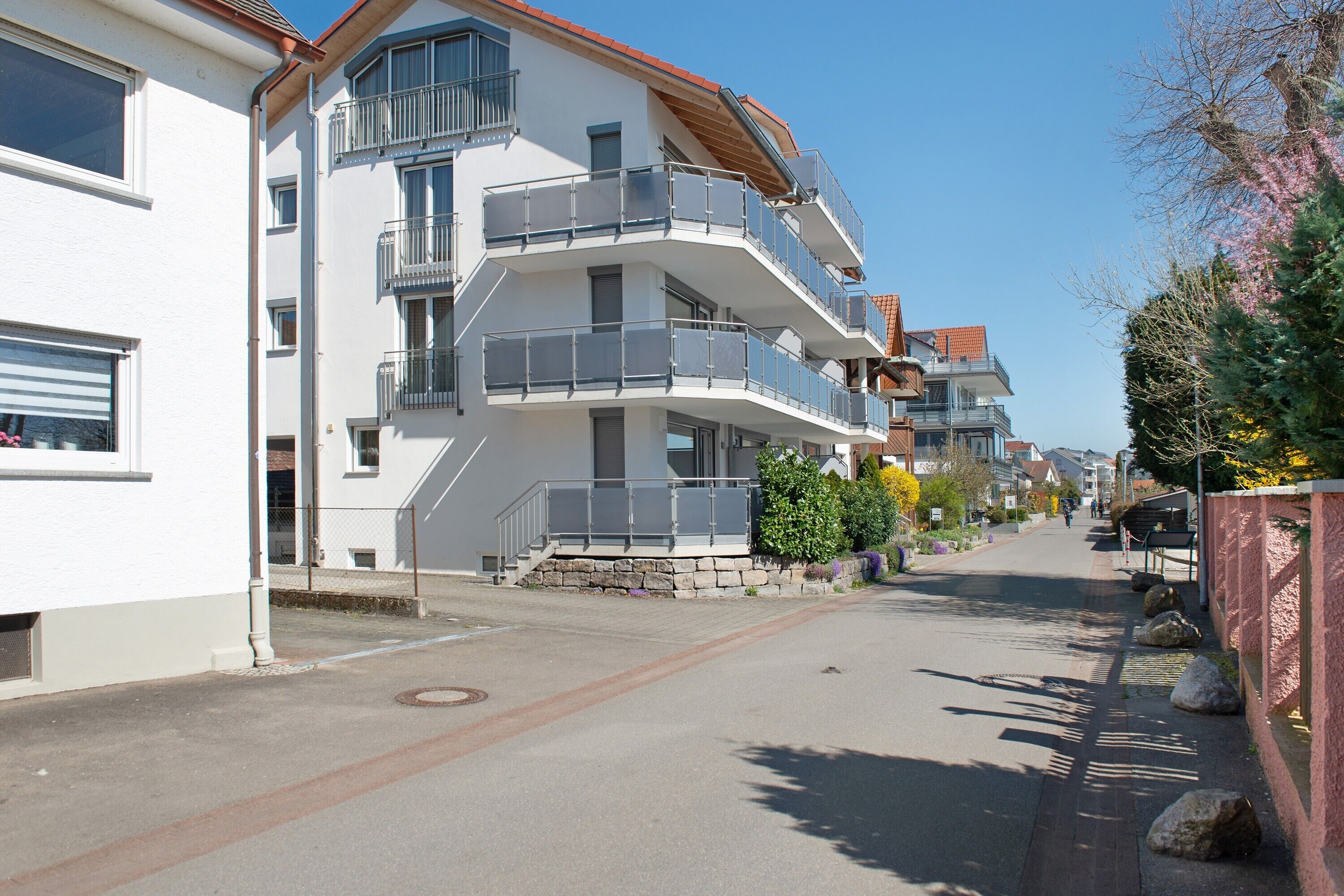 Un immeuble résidentiel à plusieurs étages, doté de balcons, situé le long d’une rue pavée, sous un ciel dégagé.
