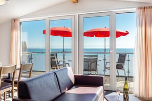 A balcony with a sofa, chairs, and red umbrellas, overlooking a body of water. - Apartment 'Dachstudio' with Shared Terrace, Shared Garden and Wi-Fi (Immenstaad am Bodensee)
