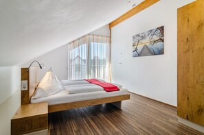 A modern bedroom with a wooden bed frame, a bedside table, a window with sheer curtains, and a wall-mounted painting. - Apartment 'Dachstudio' with Shared Terrace, Shared Garden and Wi-Fi (Immenstaad am Bodensee)