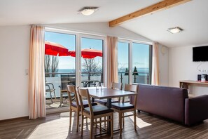 A room with a dining table, chairs, a sofa, and large windows with curtains. - Apartment 'Dachstudio' with Shared Terrace, Shared Garden and Wi-Fi (Immenstaad am Bodensee)