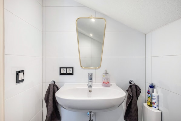 Une salle de bain avec un lavabo blanc, un miroir à cadre doré et des articles de toilette disposés sur le côté.