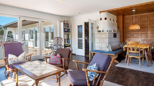 Een ruime woonkamer met houten vloer, een eettafel met stoelen, een boekenkast en een groot raam met uitzicht.