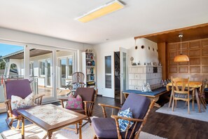 A spacious living area with a wooden floor, a dining table with chairs, a bookshelf, and a large window with a view.