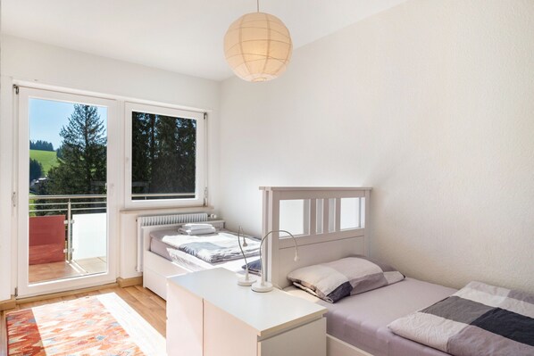 A bedroom with a bed, bedside table, lamp, and a view of a balcony.
