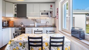 Een moderne keuken met witte kasten, een magnetron en een eettafel met stoelen.