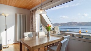 A dining area with a table, chairs, a vase with flowers, and a view of the water. - Apartment '8, 53 sqm, Directly on Lake Constance with Lake Access (Bodman-Ludwigshafen)