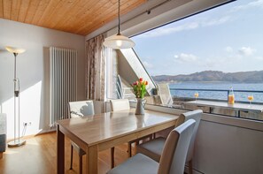 Uma sala de jantar com uma mesa, cadeiras, um vaso com flores e vista para a água.