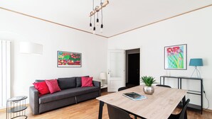 A modern living room with a grey sofa, red cushions, a wooden dining table, and two framed artworks. - Suite Duomo View 47 (Como)