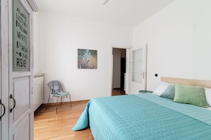 Un dormitorio con cama, una silla, un radiador y una puerta que da a otra habitación.