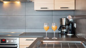 A modern kitchen with two glasses of orange juice on a counter, a coffee maker, and a digital clock displaying 4:03. - Apartment '7, 62sqm' with Large Sunny Balcony and Direct Lake Access (Bodman-Ludwigshafen)