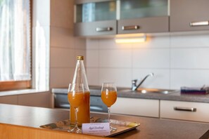 Una encimera de cocina con una botella y dos vasos de zumo de naranja, una tarjeta de identificación y una ventana con cortinas.