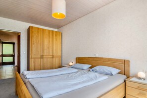 Quarto com cama de madeira, mesa de cabeceira com abajur e guarda-roupa.