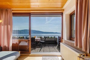 A room with a bed, a table with chairs, a view of the sea, and a window with curtains.